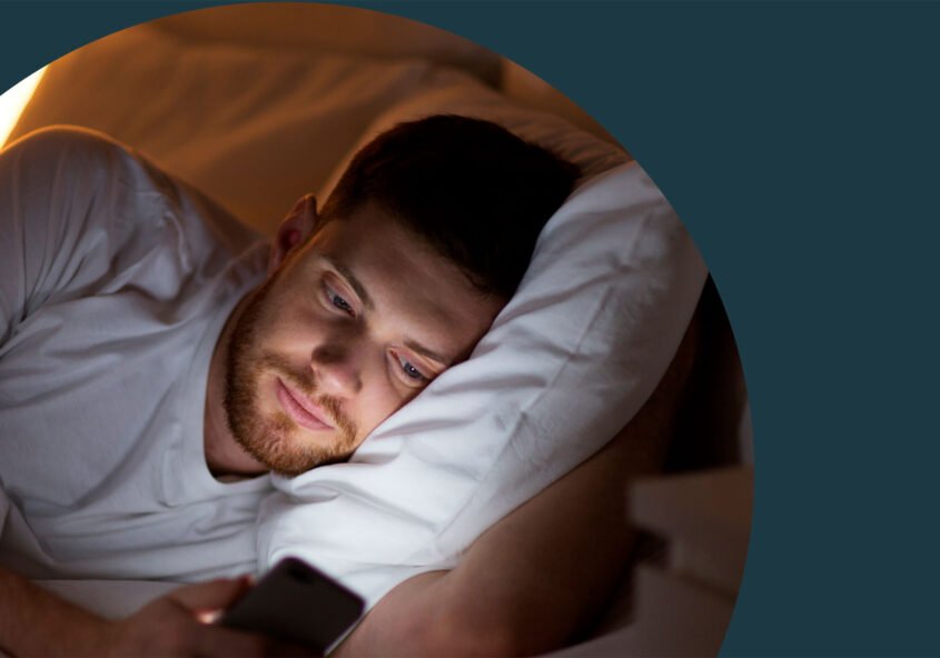 Ein Mann liegt im Bett und schaut im dunkeln auf sein Smartphone.