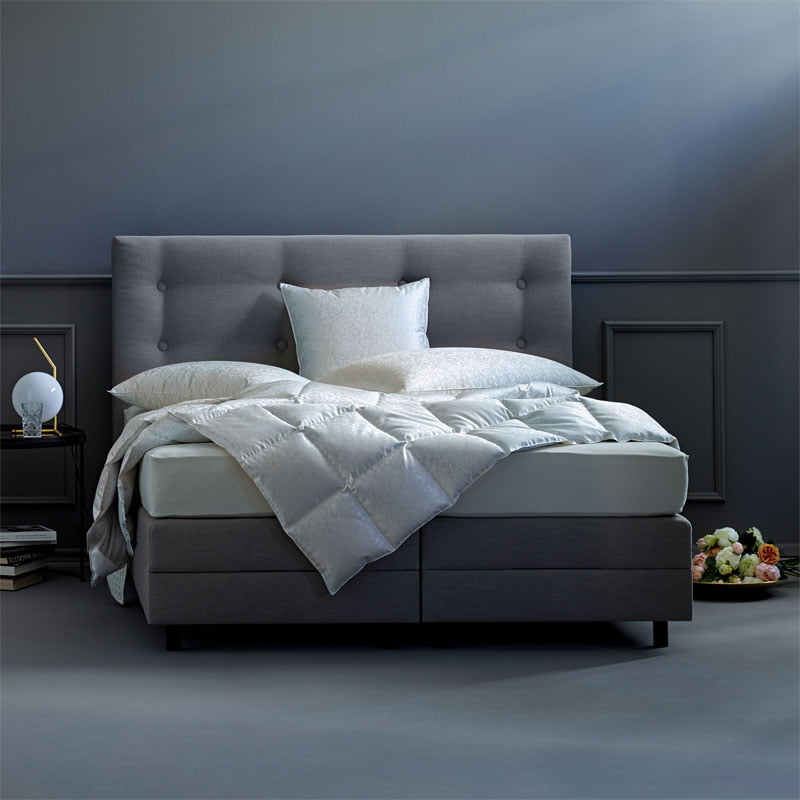 Ein Boxspringbett in grau und Kissen und Duvets die mit Eiderdaunen gefüllt sind.