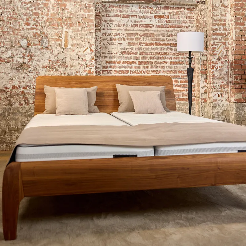 Ein Bett aus Holz steht in einem Backstein-Gebäude.