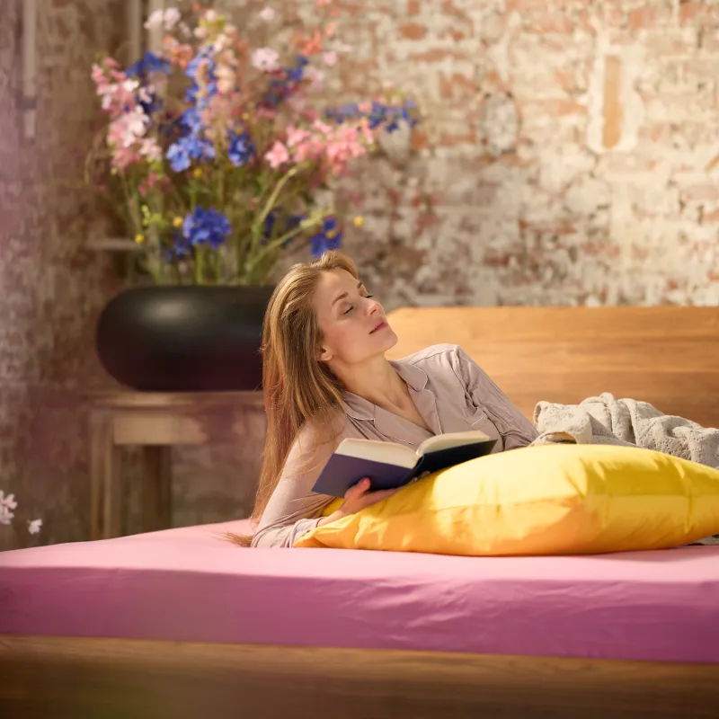 Ein Frau liest entspannt ein Buch im Bett.